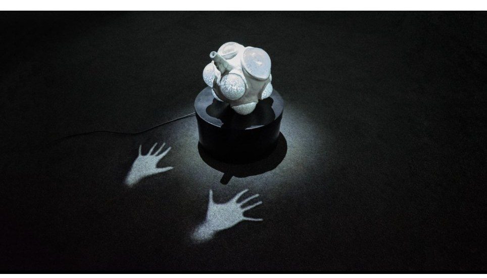 Nexus installation — glowing white device on a black pedestal with handprints